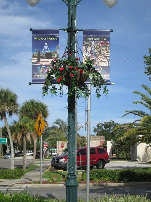 Photo of a flower basket with red flowers inside, hanging from a light pole.
