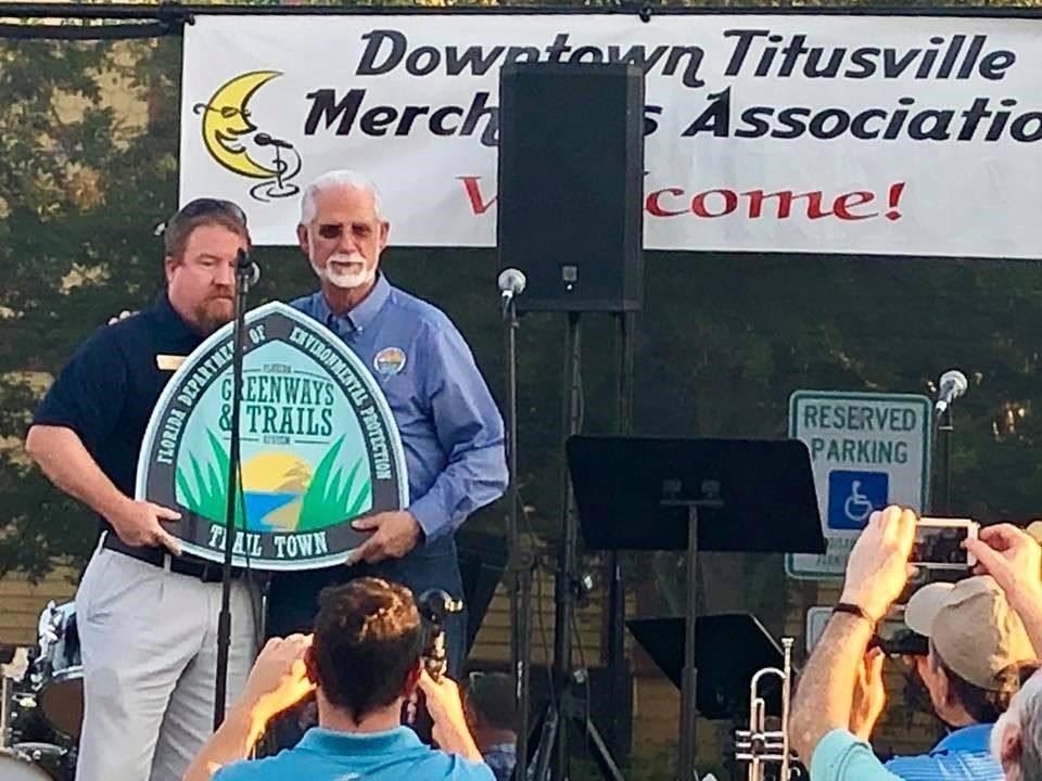 Photo of Mayor Johnson receiving a signs that says Trail Town from another man.