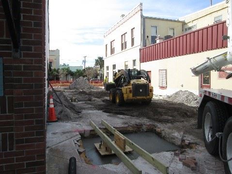 Photo of construction equipment in a court between two buildings, with the pavement torn up.